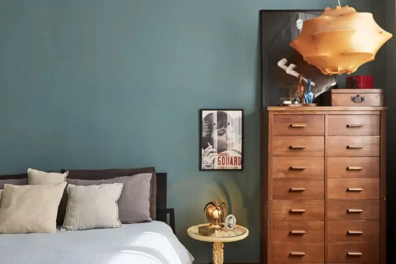 Un'elegante camera da letto con pareti color ottanio, un letto con cuscini in lino e un comò in legno. L'abbinamento colori camera da letto è sofisticato e rilassante.