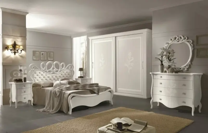 Elegante camera da letto bianca con letto capitonné, armadio scorrevole e comò con specchio. Ottime idee camera da letto bianca per un ambiente raffinato.