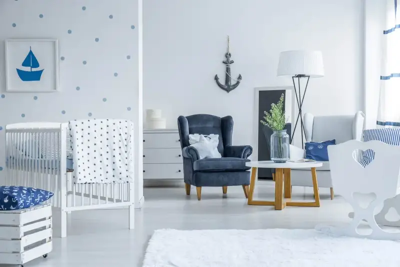 Un accogliente salotto stile marinaro con culla, poltrona blu e decorazioni a tema nautico.
