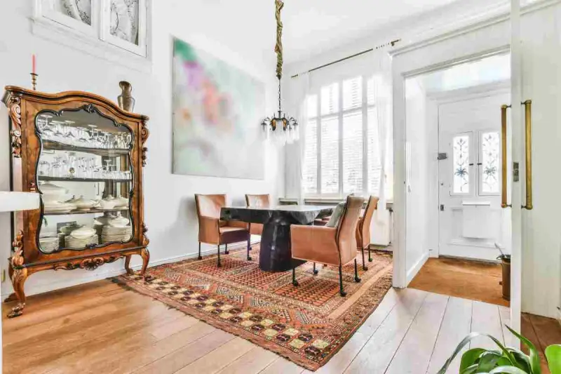 Soggiorno con arredamento misto moderno e antico: vetrina in legno intarsiato, tavolo scuro con sedie in pelle, tappeto persiano e quadro astratto.